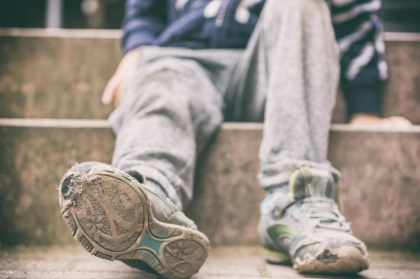 Nærbilde av et barn som sitter på en steintrapp, med grå bukser og slitte joggesko. - Klikk for stort bilde